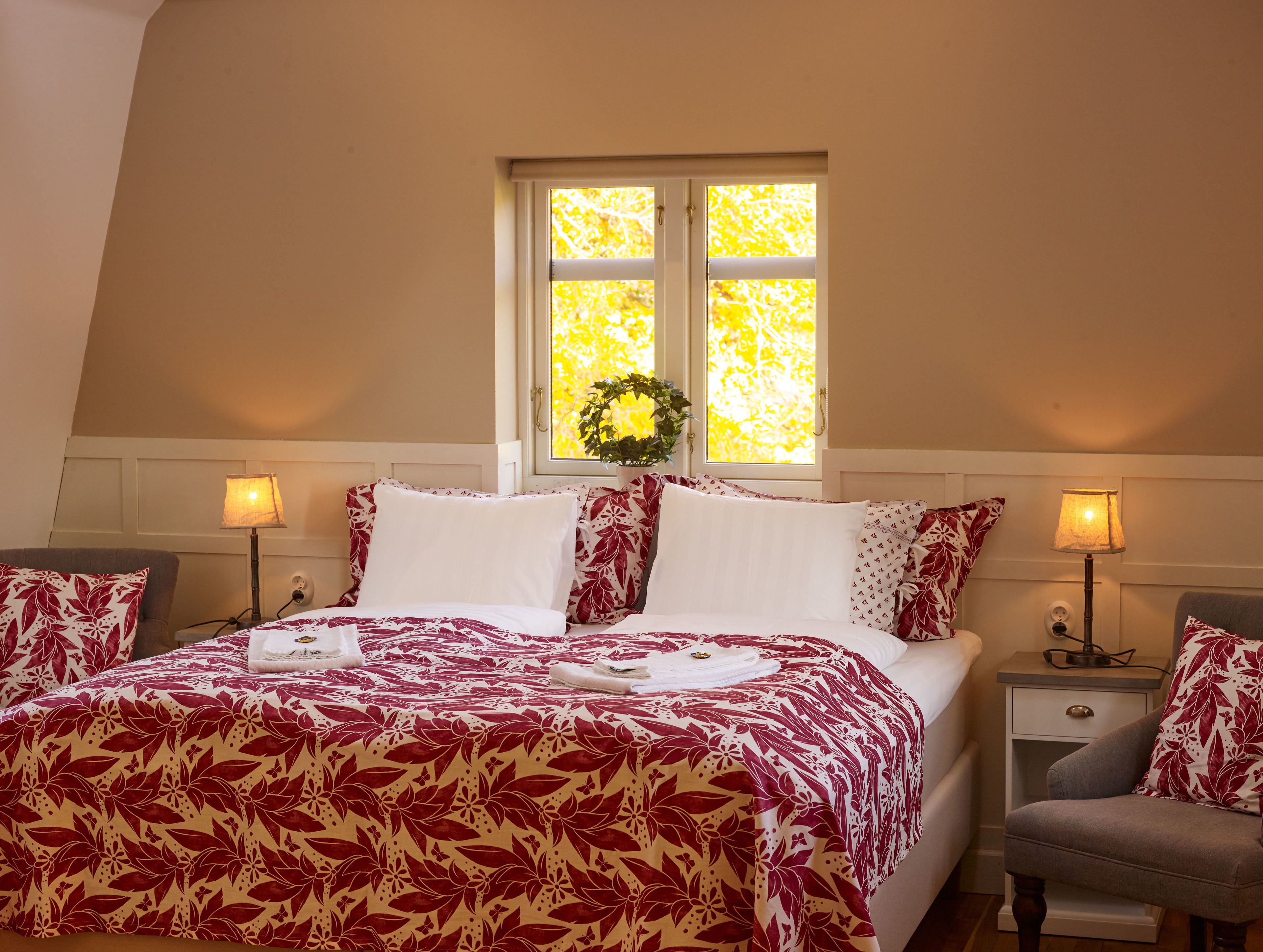 Quarto com cama grande, duas mesas de cabeceira, janela com vista e uma cadeira pequena.