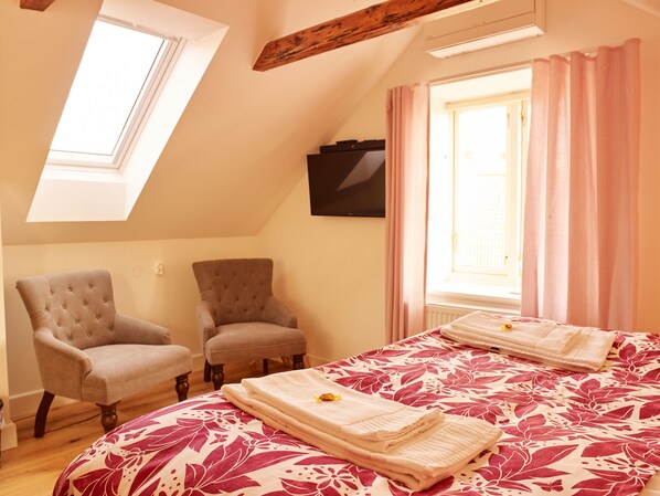 A bedroom with a sloped ceiling, two armchairs, a bed with a floral bedspread, and a window with curtains. - MillasVilla (Lund)