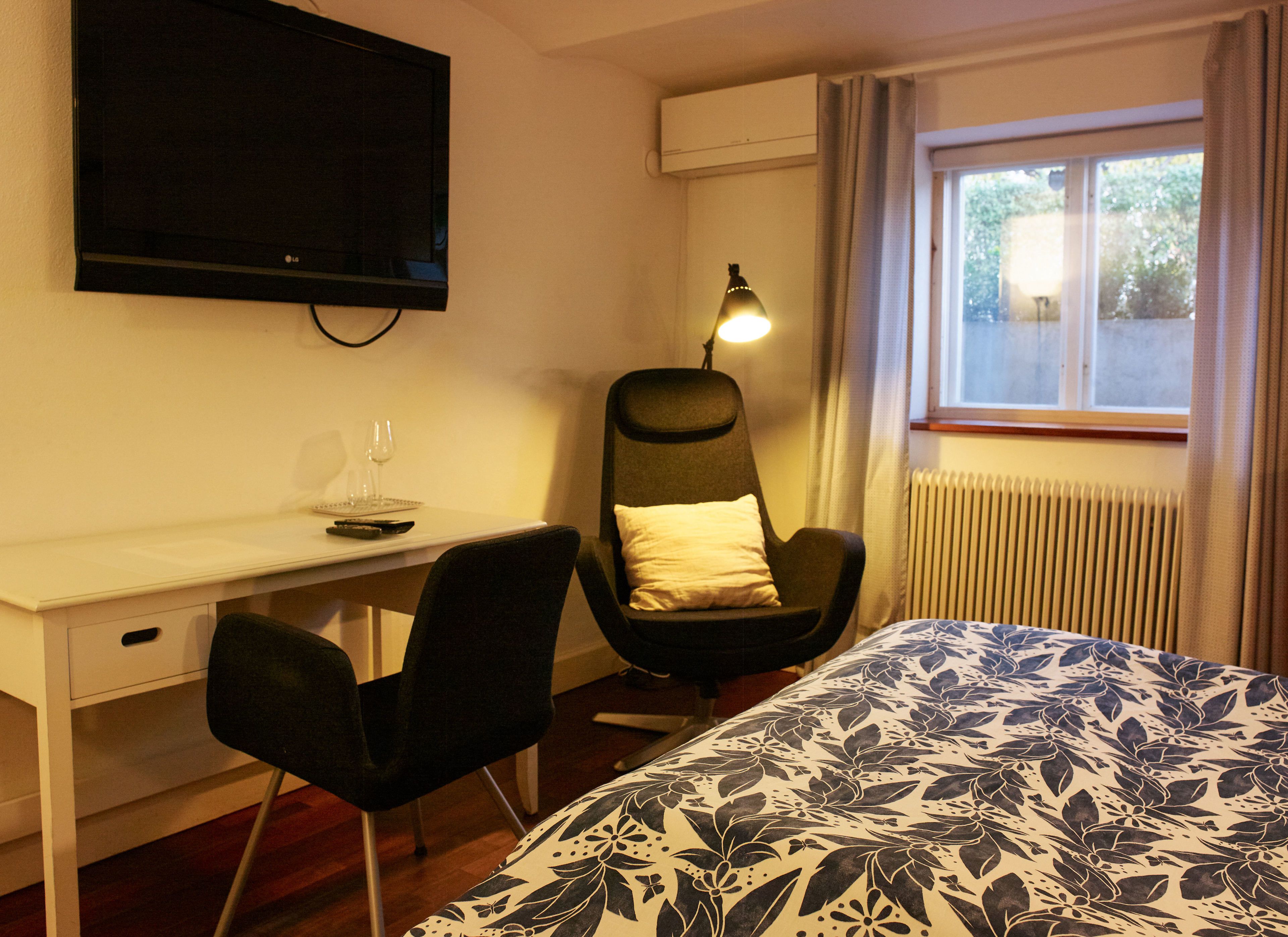 Habitación de hotel con cama, escritorio, silla, televisor, lámpara y ventana.