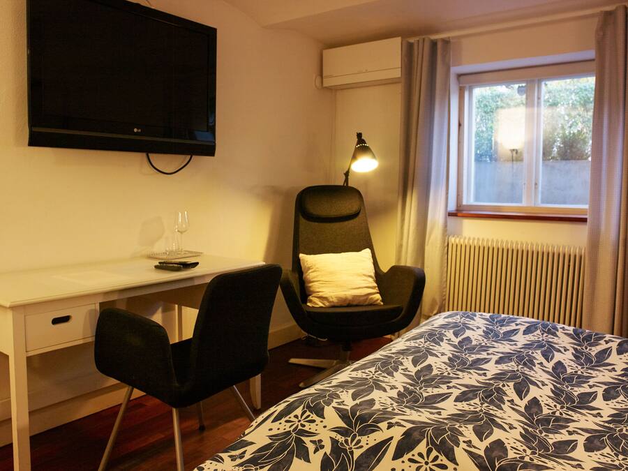 Habitación de hotel con cama, escritorio, silla, televisor, lámpara y ventana.