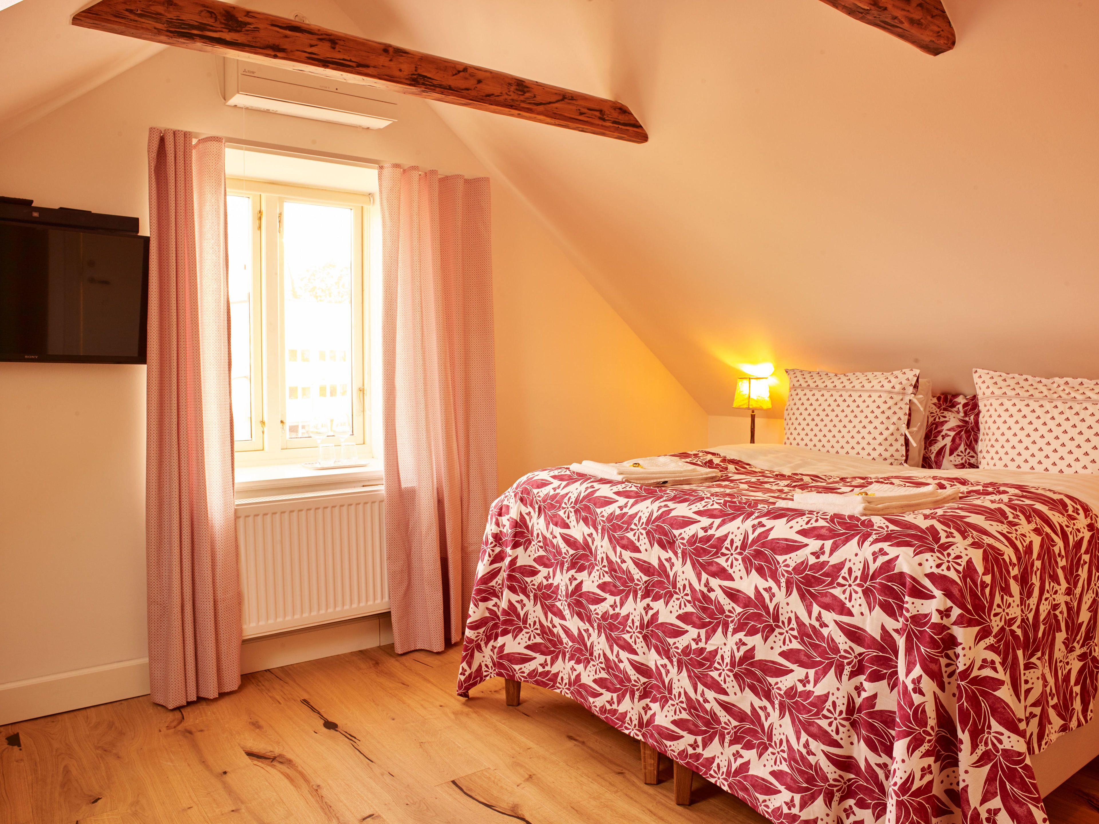 A bedroom with a bed, a window with curtains, a radiator, and a lamp.