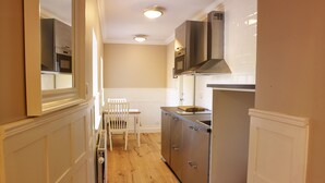 A narrow kitchen with wooden flooring, white cabinetry, and a white chair. - MillasVilla (Lund)