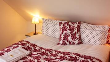 Una cama bien hecha con ropa de cama floral, una viga de techo de madera y una lámpara de noche.
