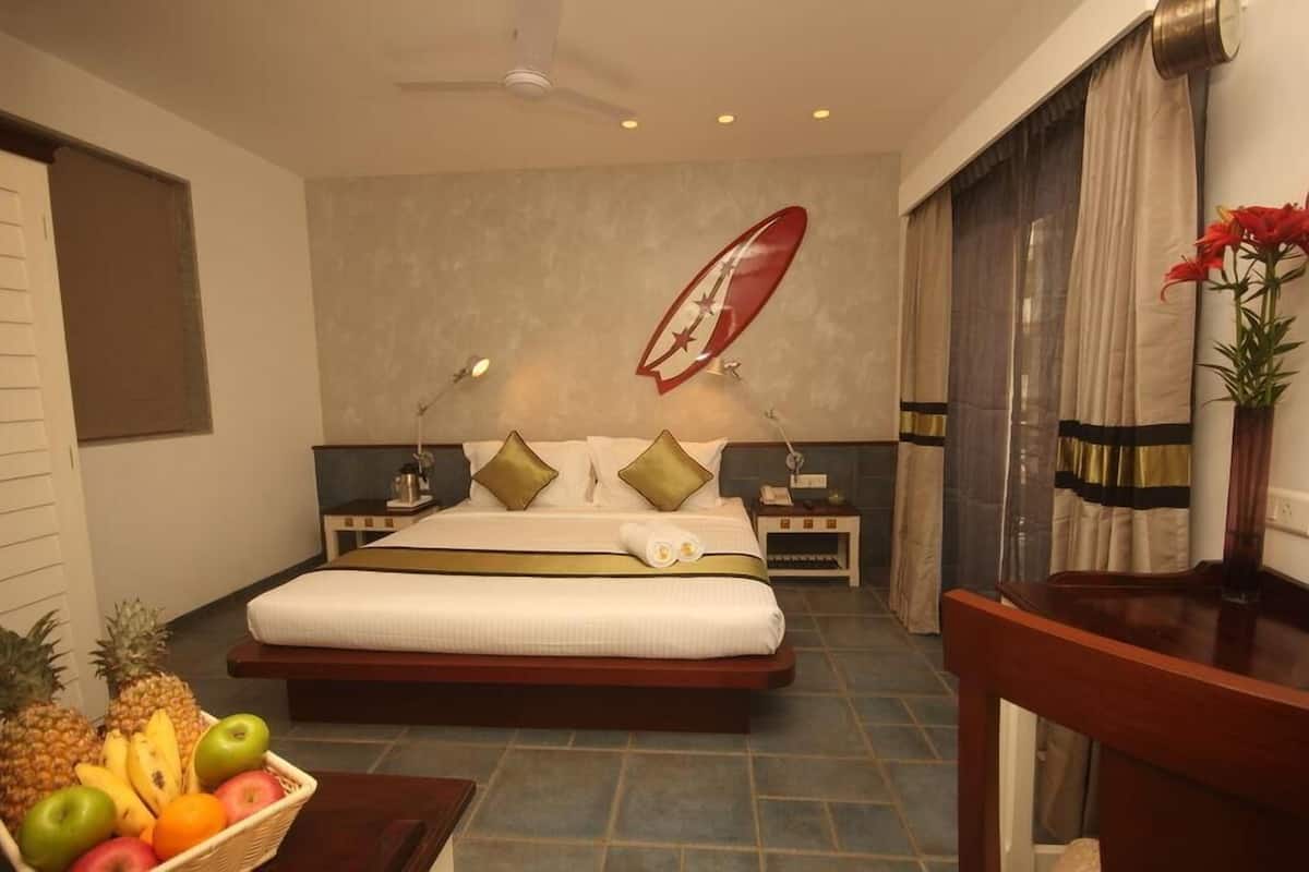 Habitación de hotel con una cama grande, un televisor de pared, una mesita con fruta y un balcón con cortinas.