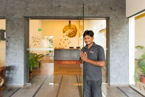 A man standing in a lobby with a reception desk, a wall with a circular design, and potted plants. - The Fern Residency Miramar (Panaji)