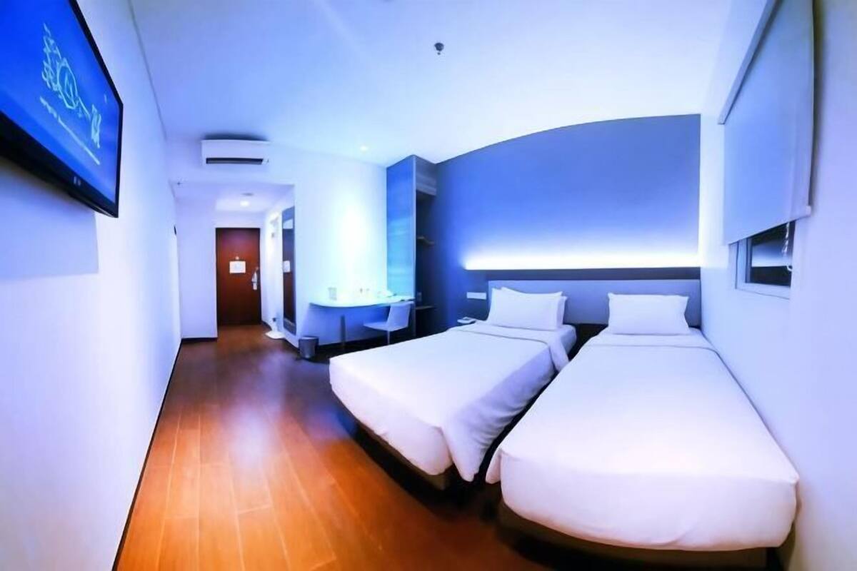 Habitación de hotel con dos camas individuales, un televisor de pantalla plana, una mesita de noche y una ventana.