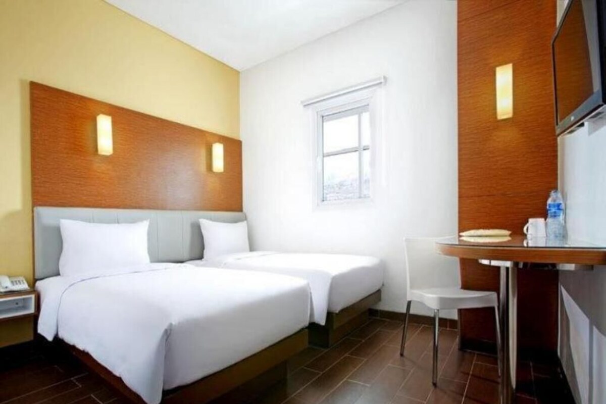 Een hotelkamer met twee bedden, een bureau, een stoel, een kleine tafel, een nachtkastje en een raam.
