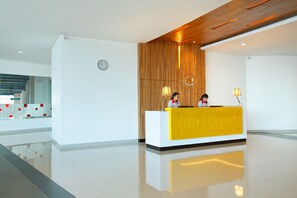 Un área de recepción moderna con una pared decorativa de madera, un mostrador amarillo y un reloj en la pared.
