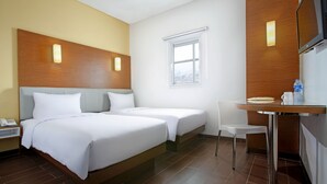 Habitación de hotel con dos camas, una mesita, una silla, un televisor y una ventana.