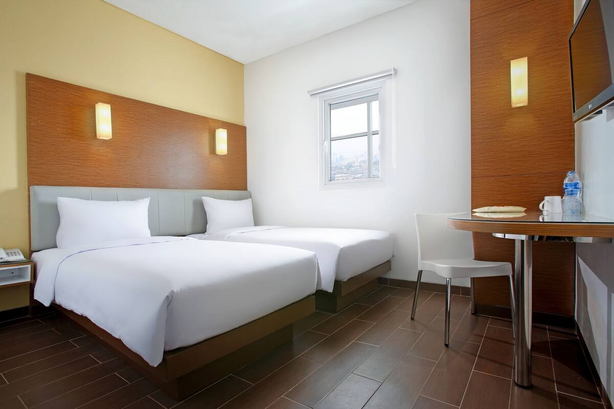 Habitación de hotel con dos camas, una mesita, una silla, un televisor y una ventana.