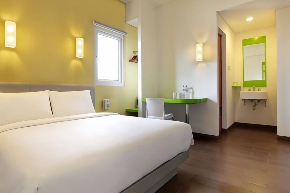 Een hotelkamer met een groot bed, een bureau met stoel, een wastafel en een spiegel.