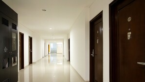 Un pasillo de hotel con diseño moderno, que presenta un largo recorrido con puertas a ambos lados, piso de baldosas impecable y una lámpara de techo luminosa.