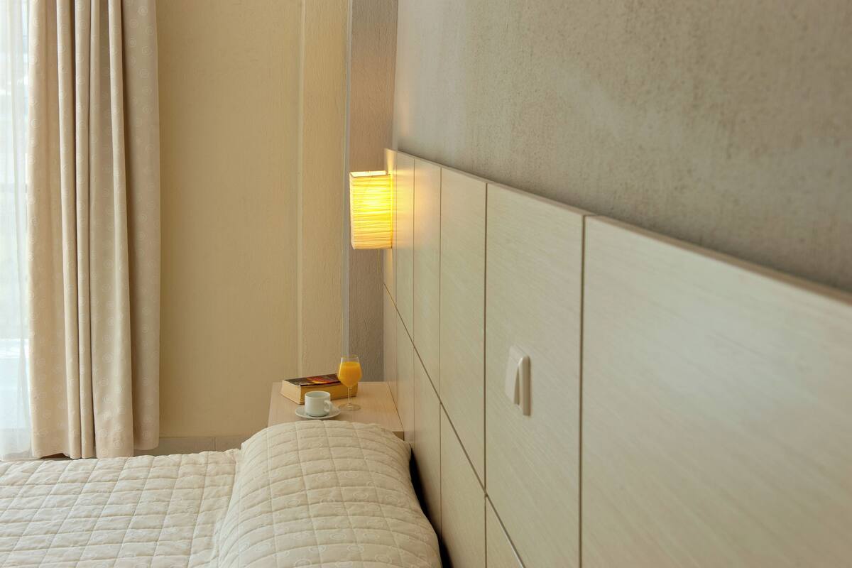 Une chambre d’hôtel avec un lit, une table de chevet sur laquelle se trouve un livre et un verre de jus d’orange, et une lampe fixée au mur.
