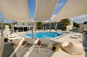 Una piscina al aire libre, sombrillas, sillones reclinables de piscina
