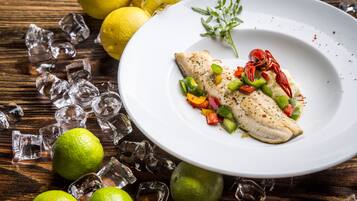 A white plate with a fish fillet, surrounded by ice cubes, lemons, and a sprig of thyme.