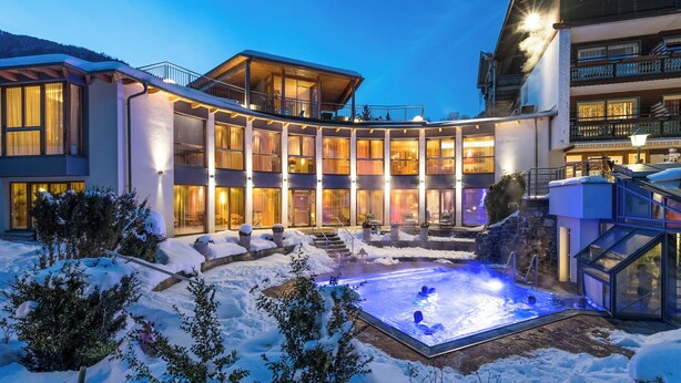 Un hotel moderno con un patio central que presenta una piscina al aire libre climatizada, rodeado de terreno cubierto de nieve y edificios de varios pisos.