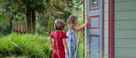 Dos niños de pie frente a un cobertizo de madera con una puerta roja.