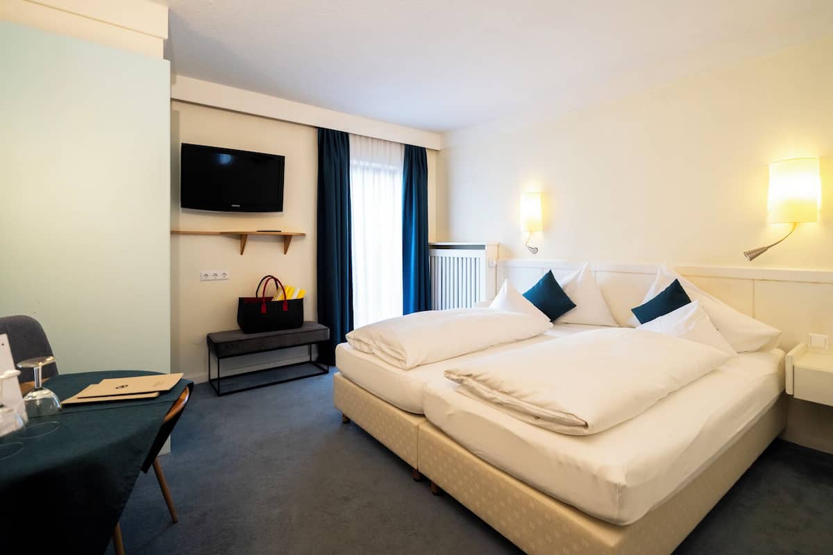 A hotel room with a large bed, a desk with a chair, a television mounted on the wall, and a nightstand with a lamp.
