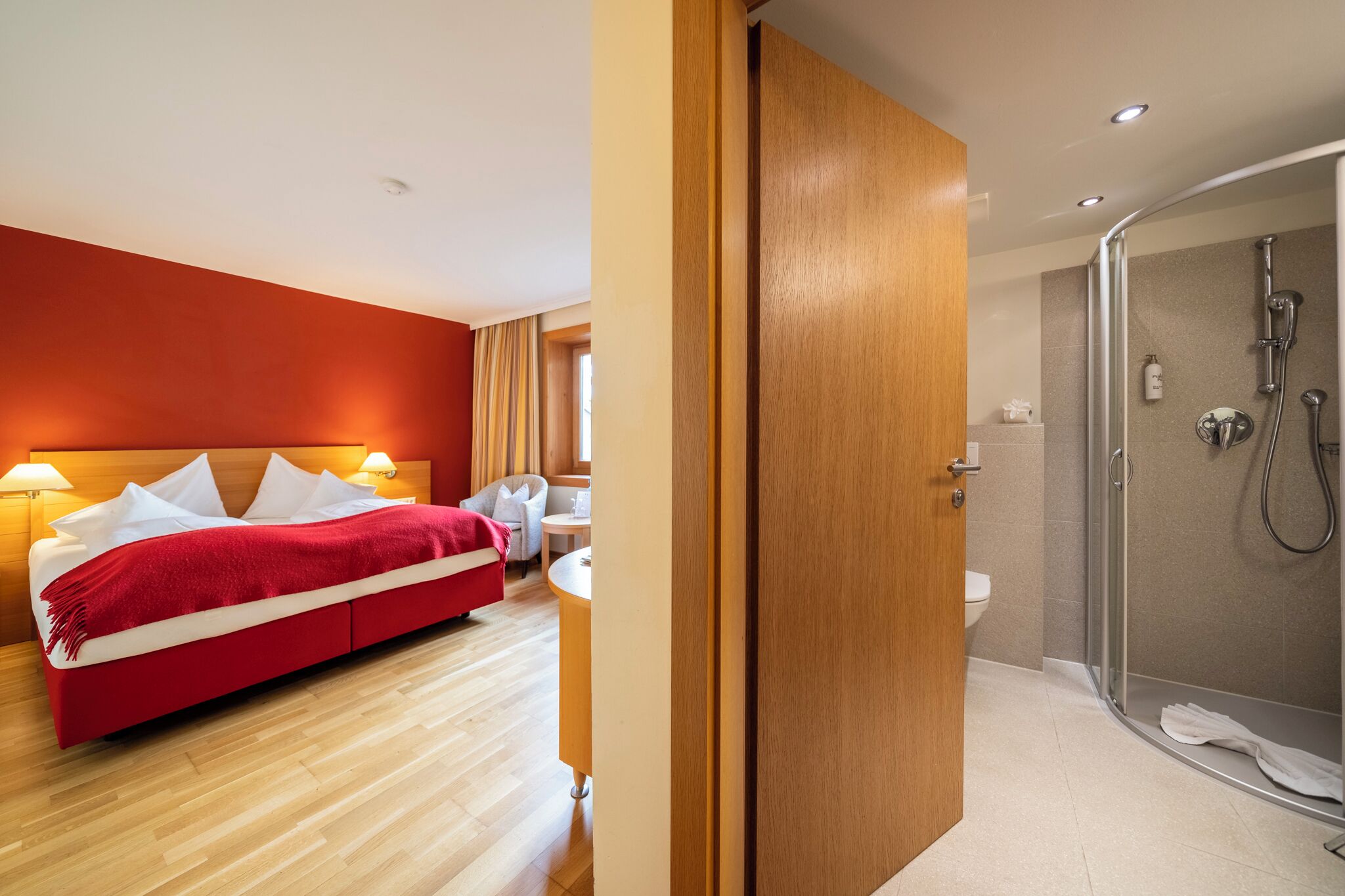 A hotel room with a bed, bedside table, and a shower area.