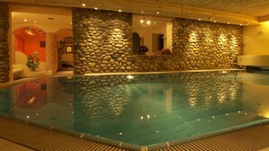 Una piscina interior con paredes de piedra y vigas de madera en el techo.