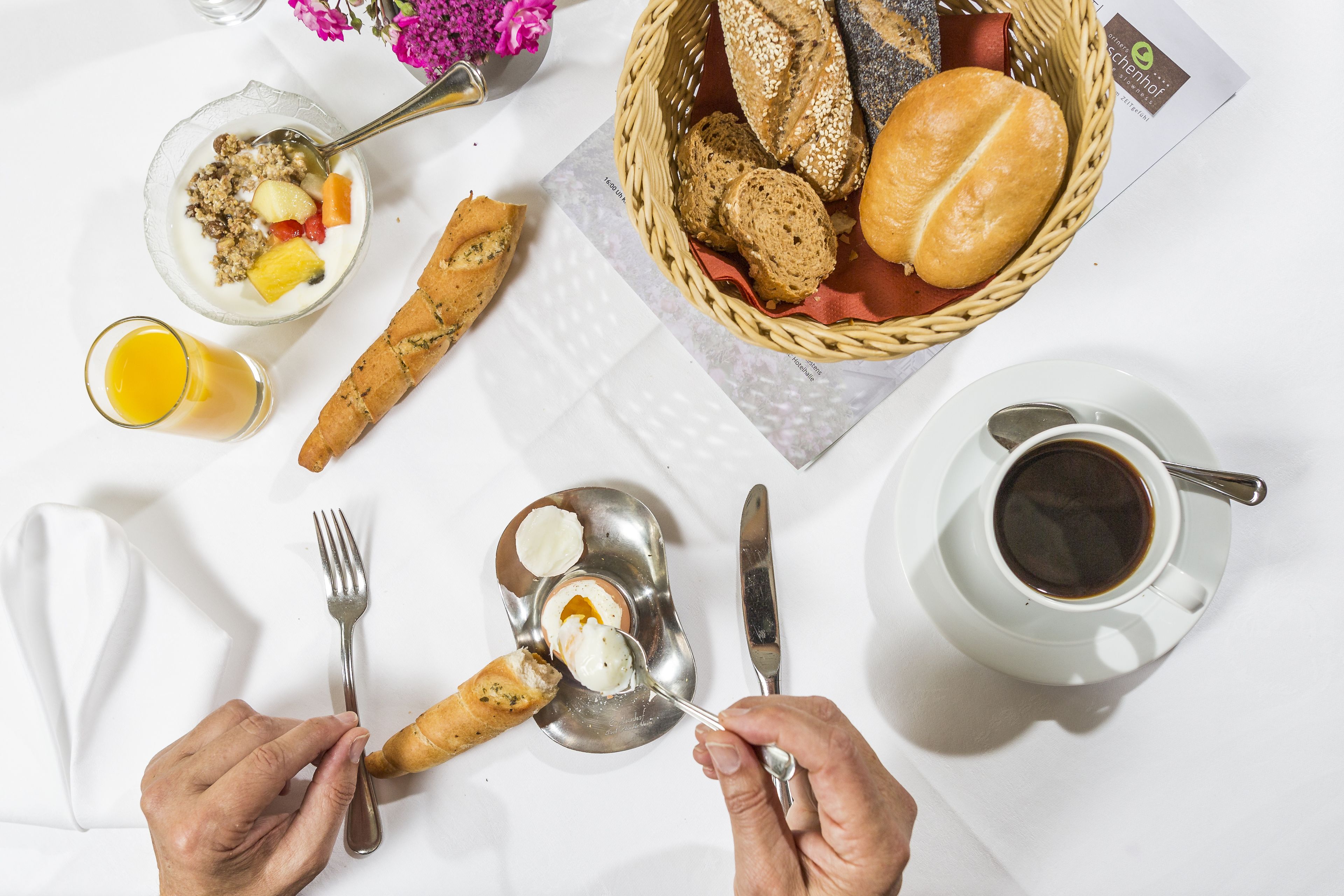 Desayuno con pan, fruta, yogur y café sobre una mesa blanca.