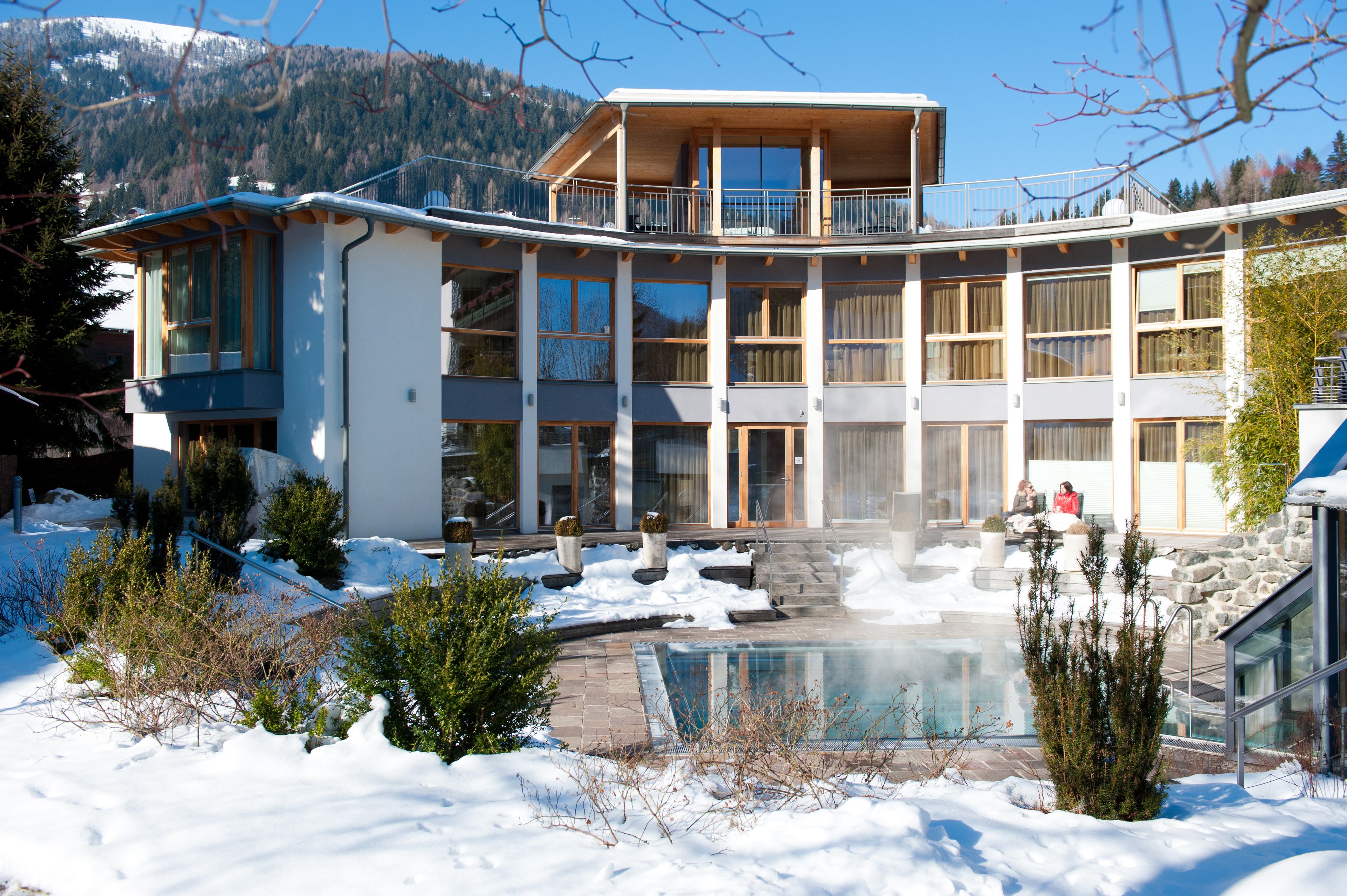 A multi-story building with a pool, surrounded by snow and trees.