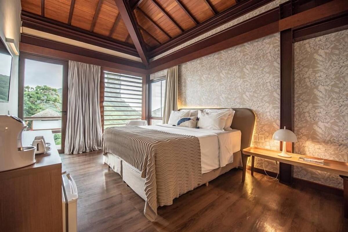 Un dormitorio con una cama grande, piso de madera, un escritorio con lámpara y una ventana con cortinas.