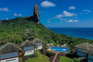 A resort with a swimming pool, a tall rock formation, and lush greenery.