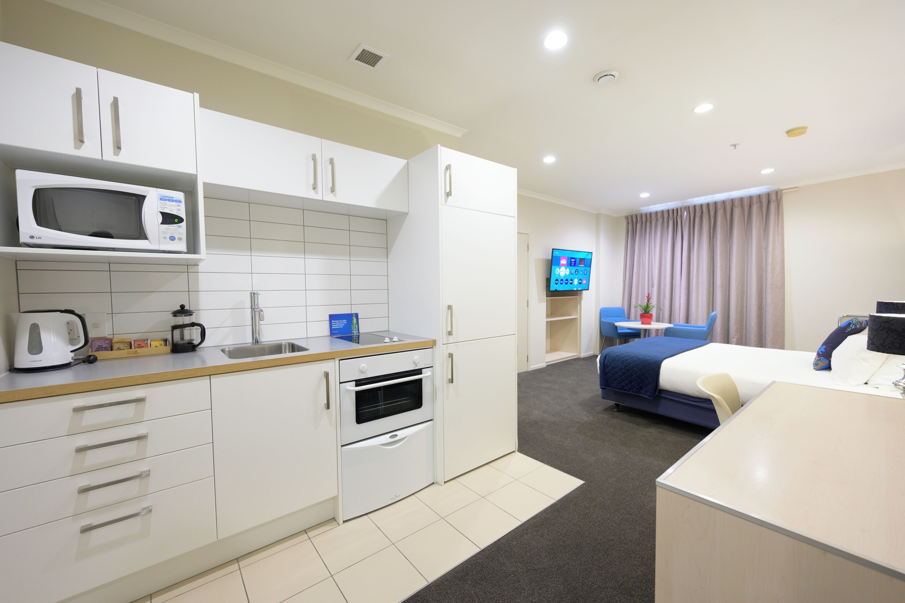 Quarto de hotel compacto com cozinha compacta, cama, televisão e banheiro.