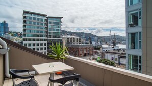 A balcony with a table and two chairs, overlooking a cityscape with modern buildings and a distant hill. - U Residence Hotel, Signature Collection by BW (Wellington)