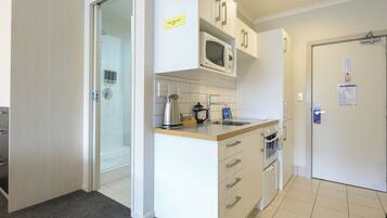 A modern kitchen with white cabinets, a microwave, a kettle, and a sink.
