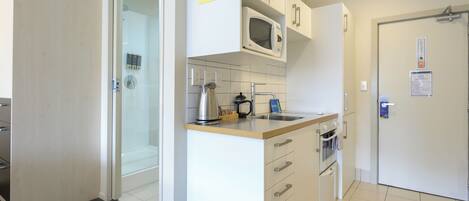 A modern kitchen with white cabinets, a microwave, a kettle, and a sink.