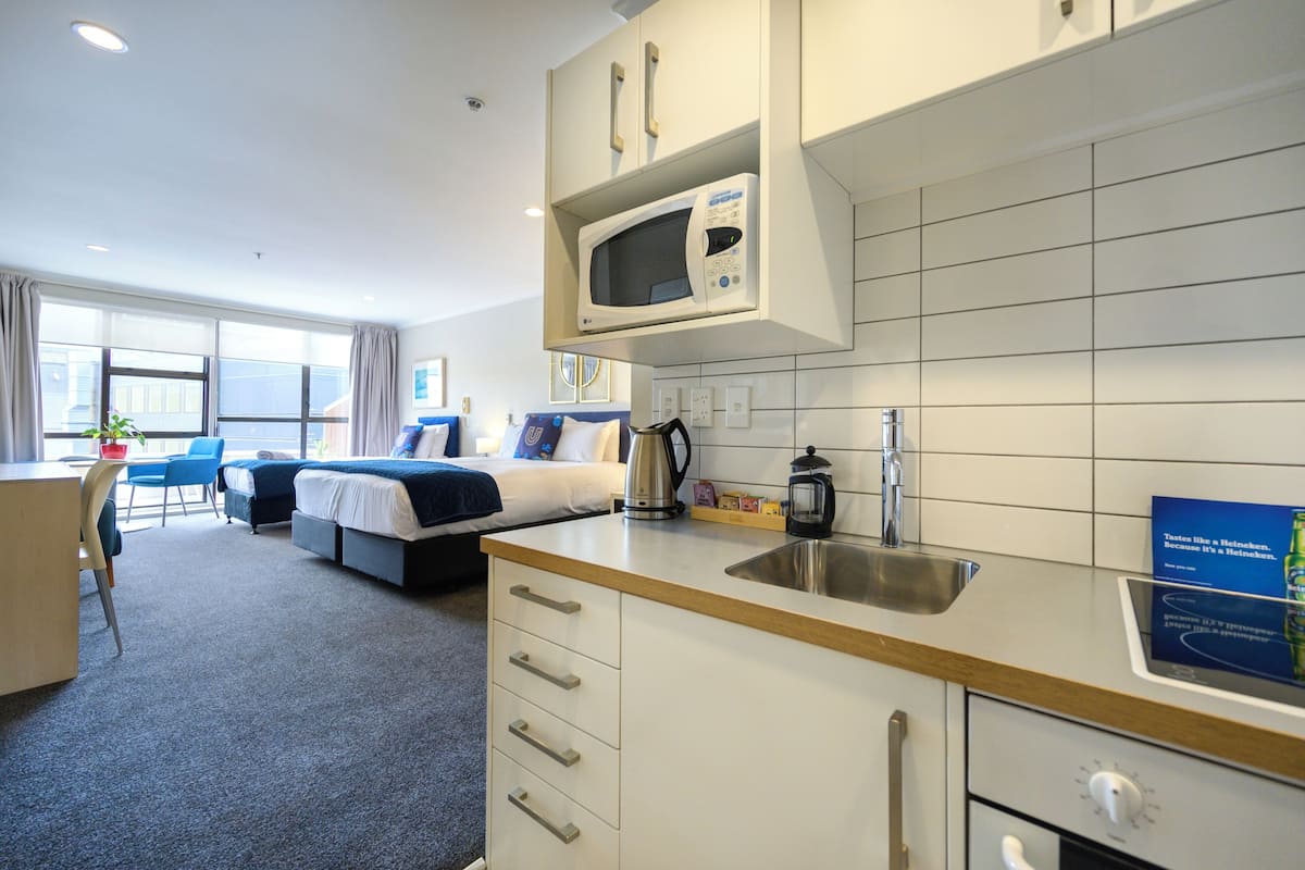A hotel room with a kitchenette, a bed, a desk, and a chair.