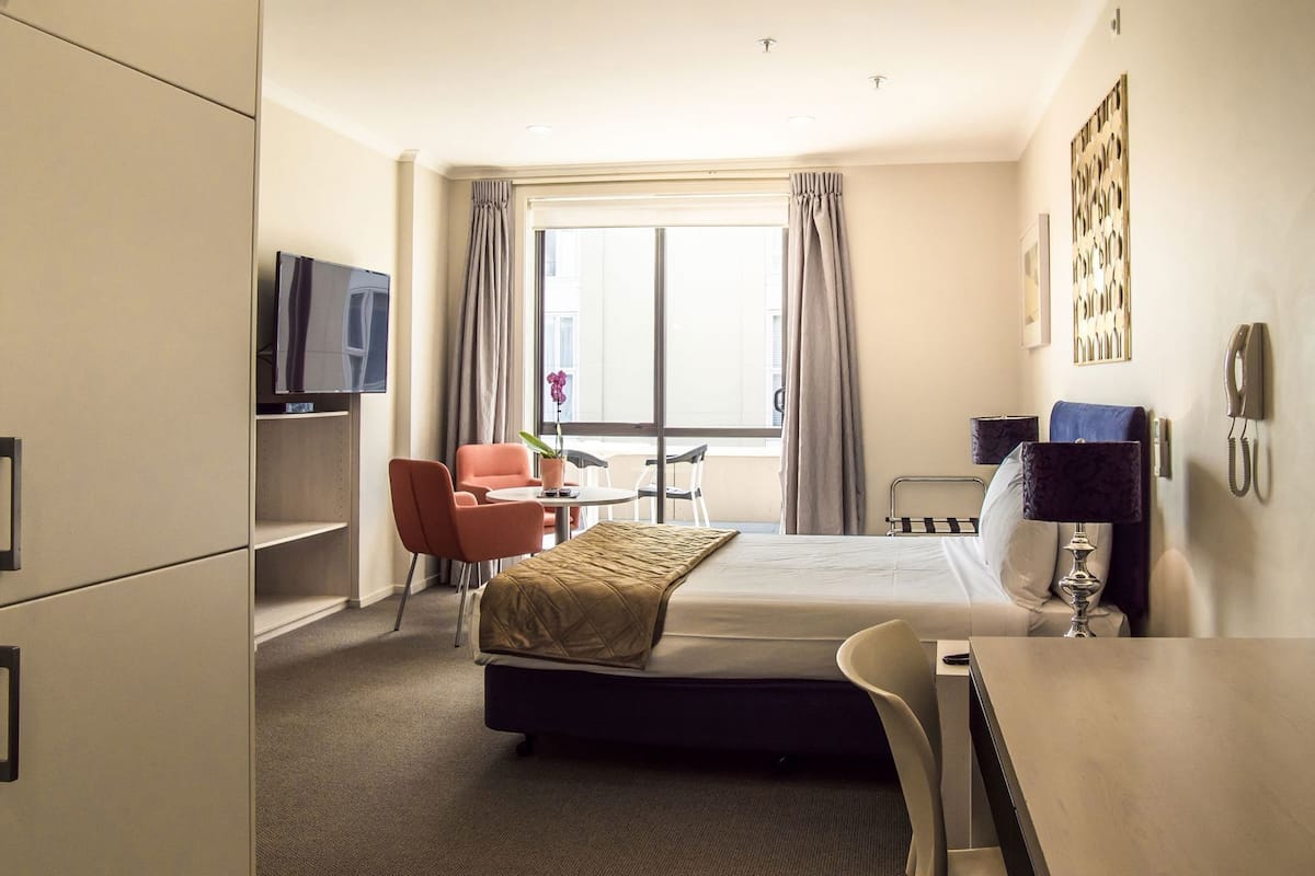A hotel room with a bed, a desk, a chair, a television, a window with curtains, and a phone.