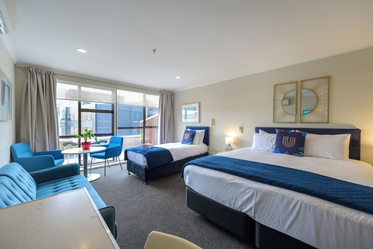 A hotel room with two beds, a sofa, a small table, and a window with curtains.