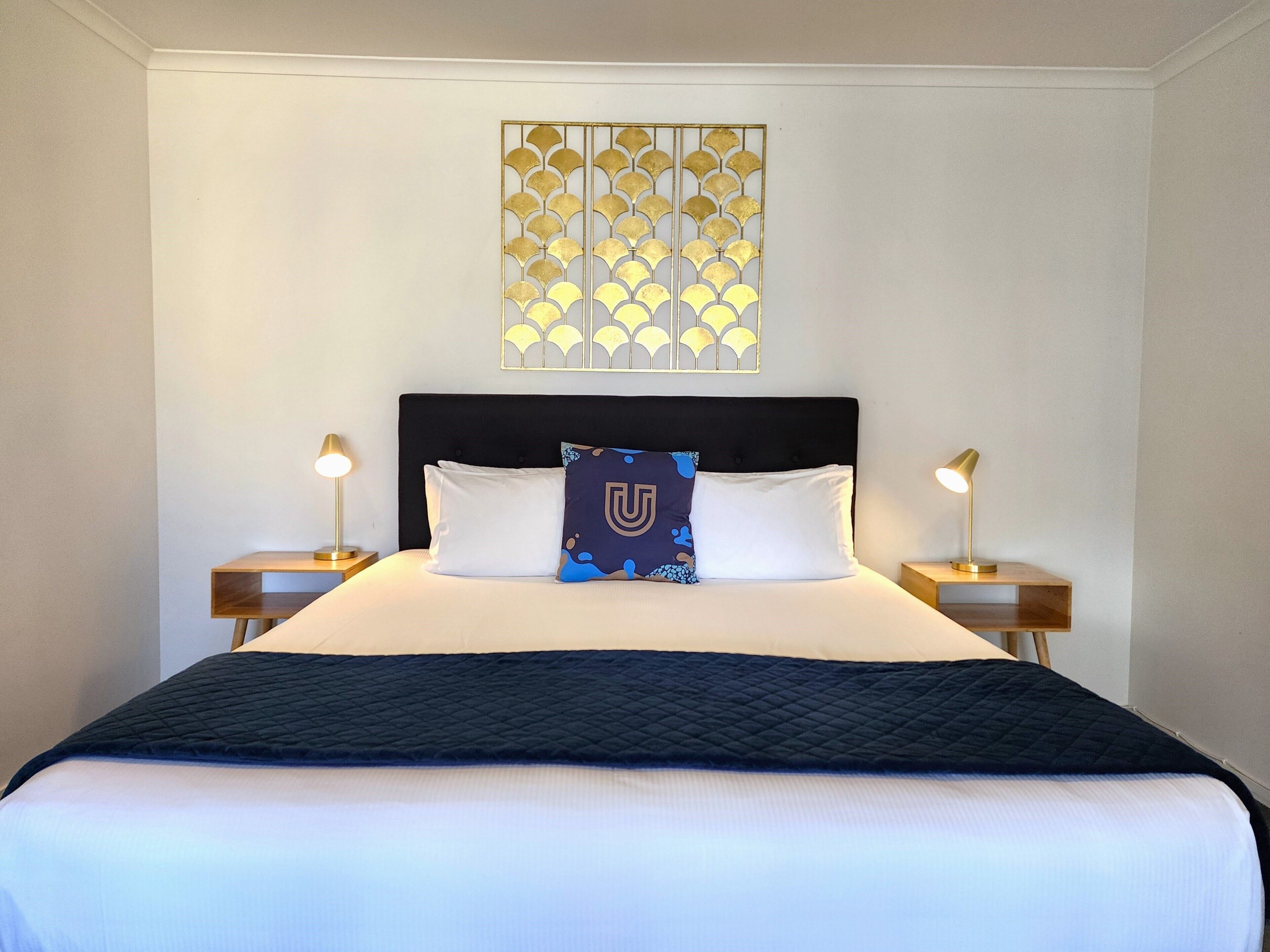 Una cama bien hecha con un cabecero negro, dos lámparas de noche y un adorno decorativo encima.