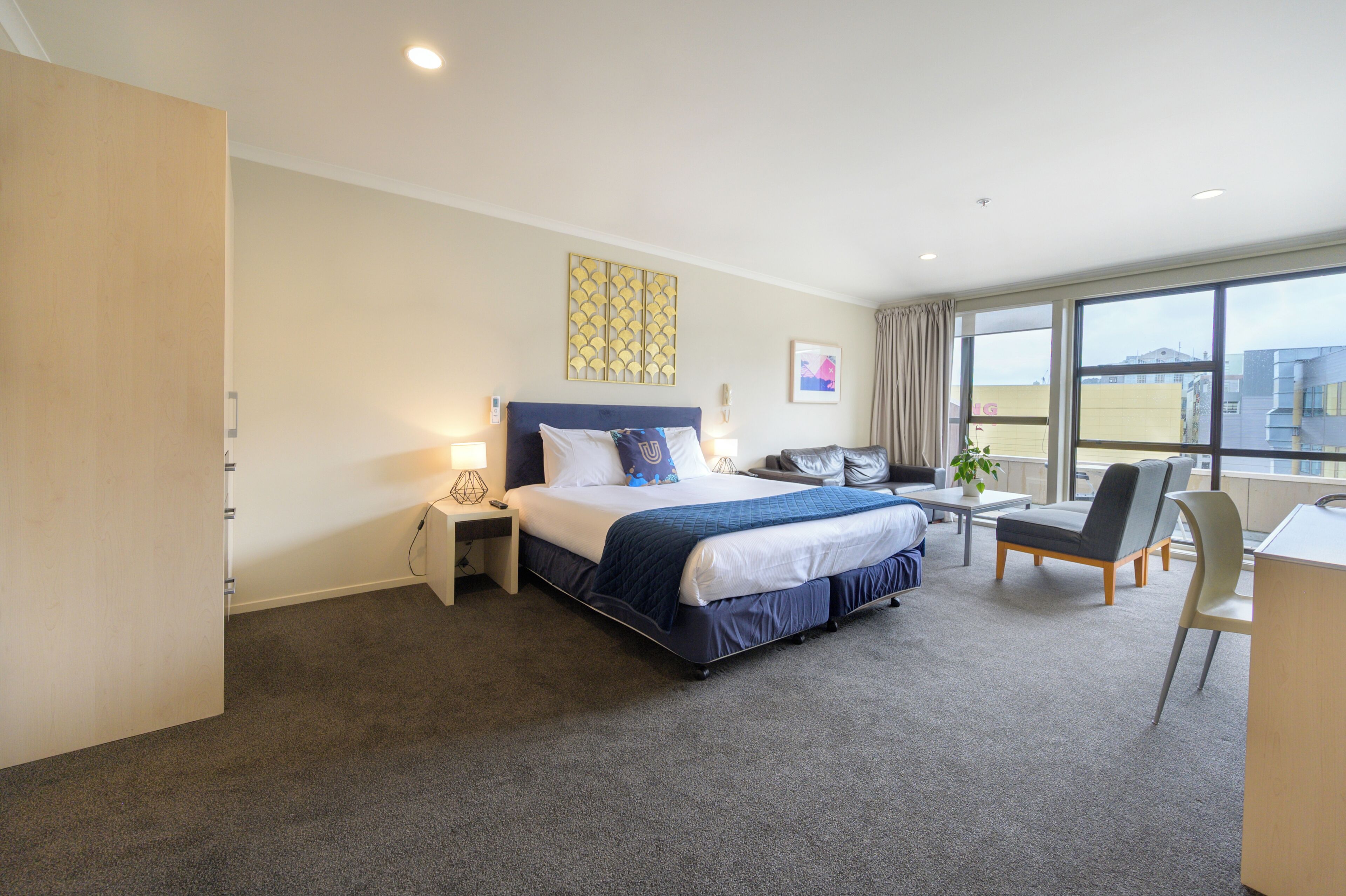A hotel room with a large bed, bedside tables, a desk, a chair, and a window with a city view.