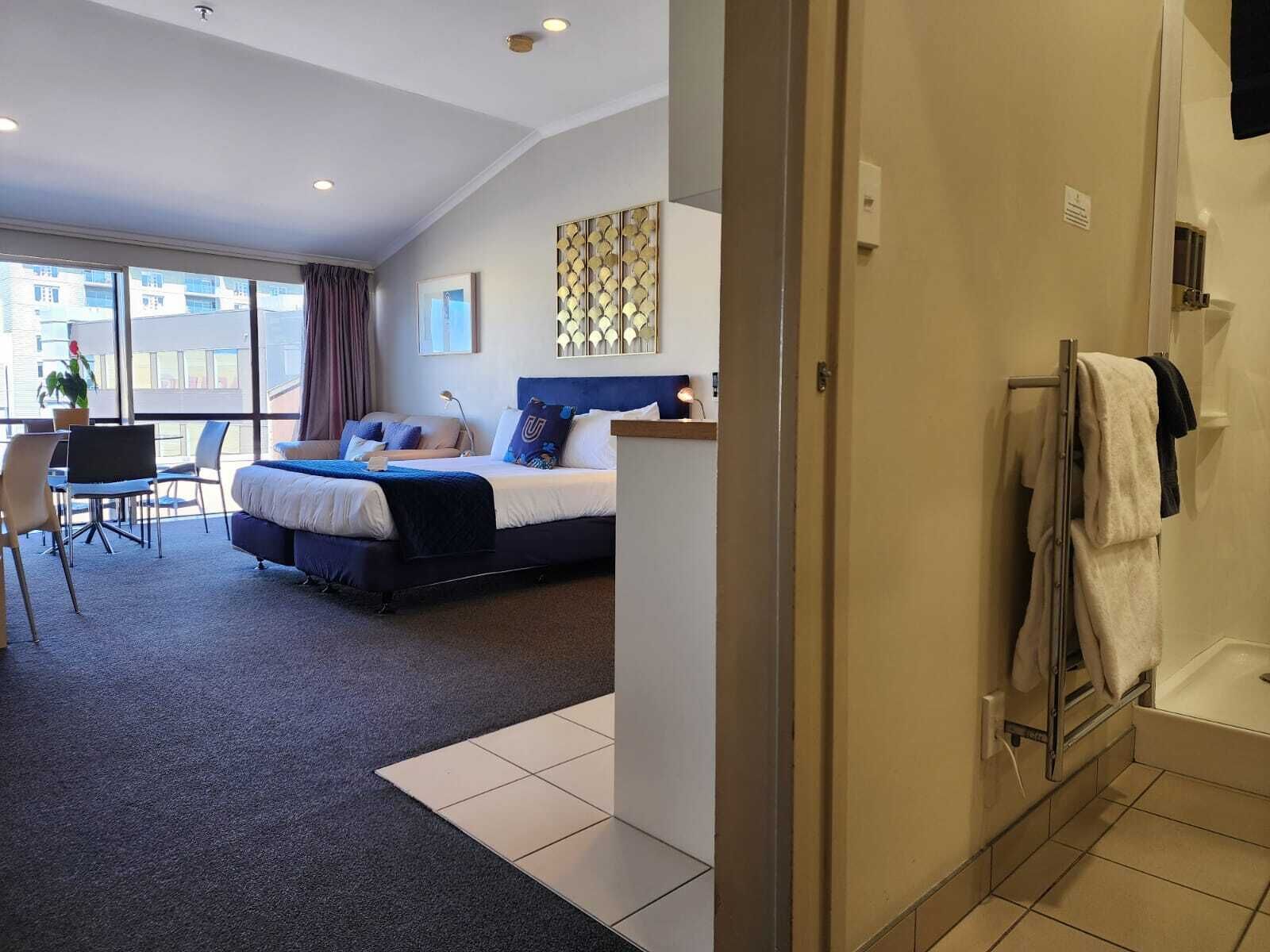 A hotel room with a bed, a desk, and a view of the city.