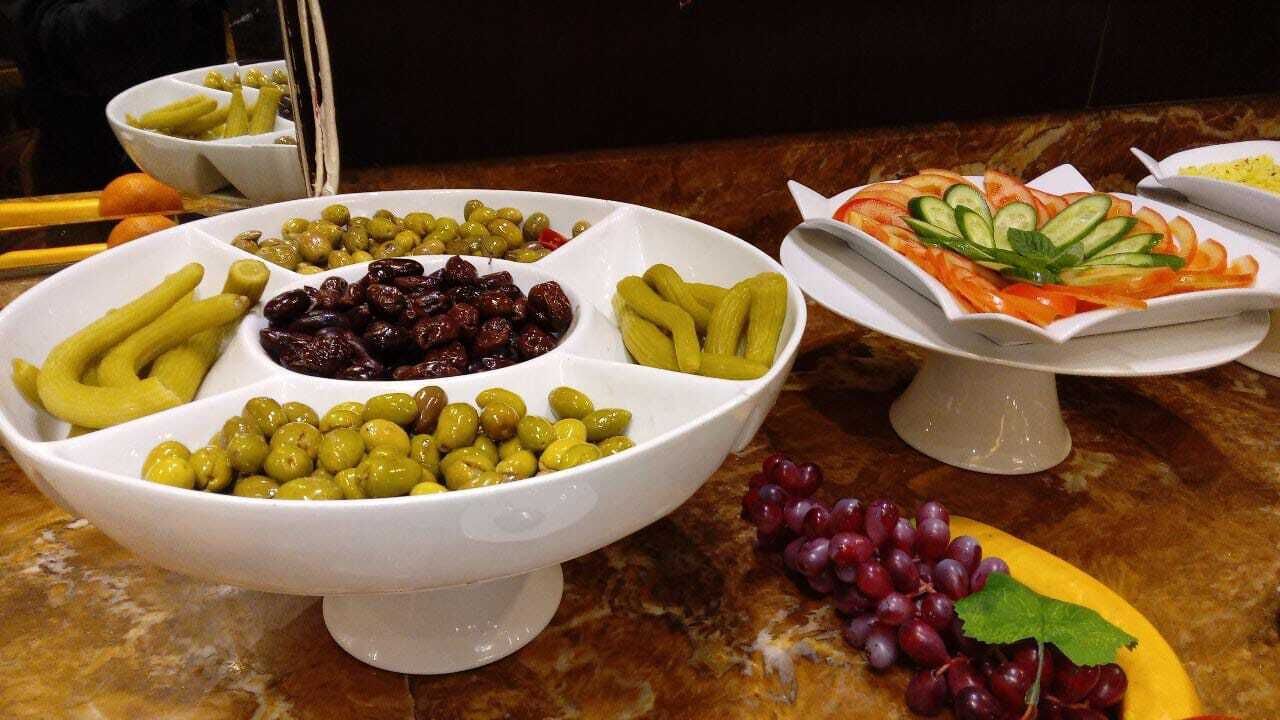 A buffet table with various food items including olives, pickles, and grapes.