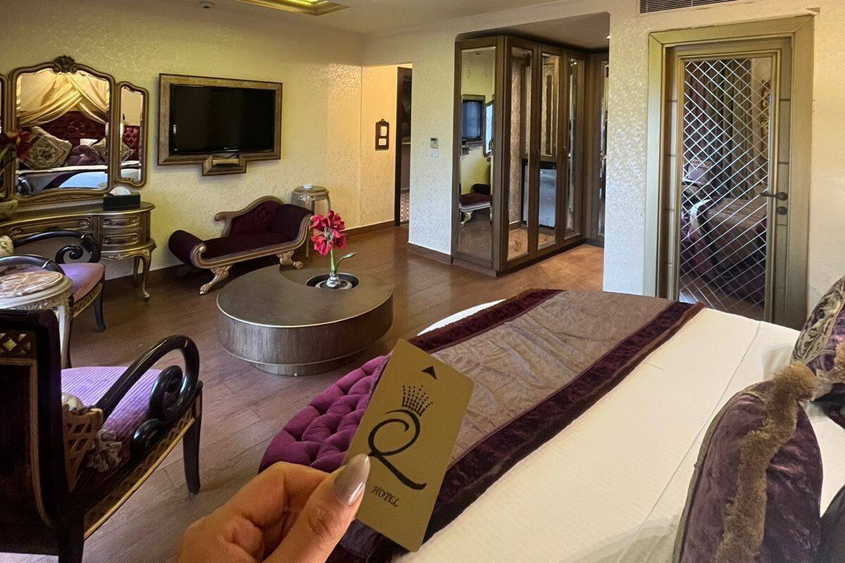 A hotel room with a bed, a round coffee table, a TV, a mirror, and a door leading to a balcony.