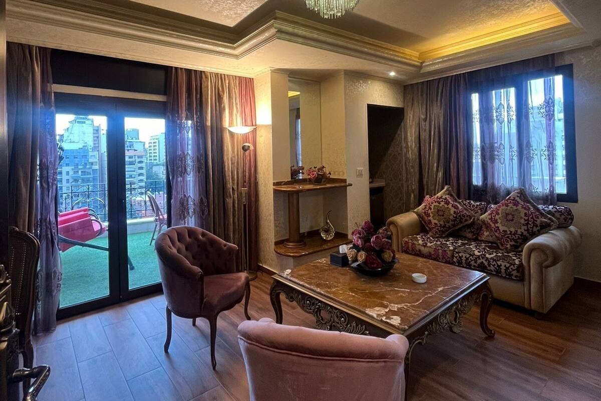 A spacious living room with a large window, a chandelier, a sofa, and a dining table.
