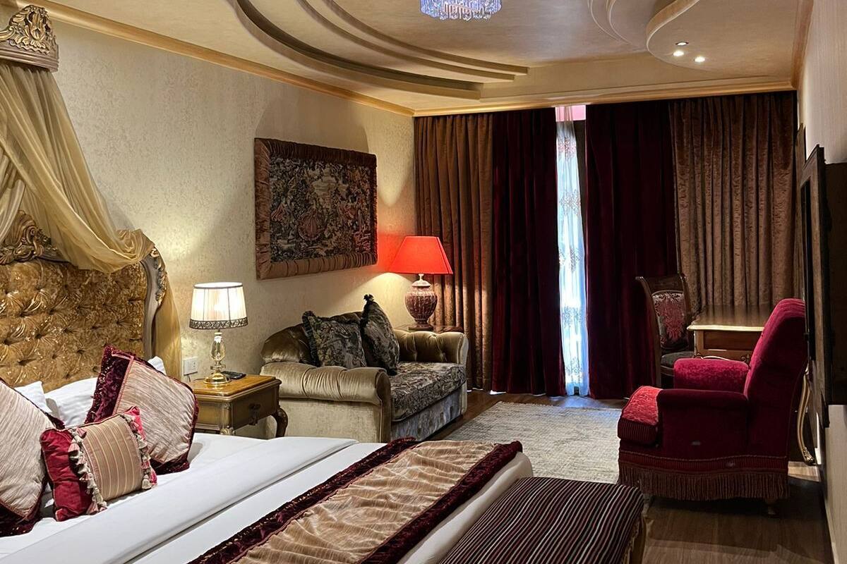 A luxurious bedroom with a large bed, a chaise lounge, a red armchair, and a chandelier.