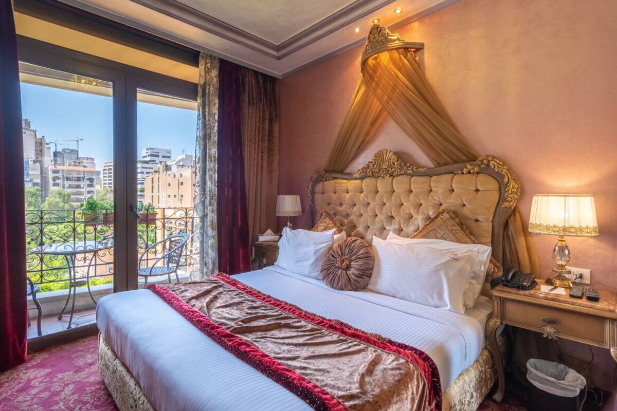 A hotel room with a large bed, a canopy, a view of the city, and a balcony with chairs.