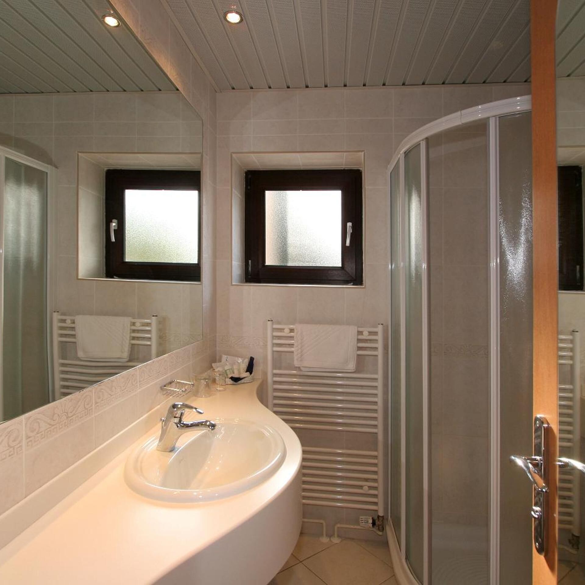 A bathroom with a large sink, two mirrors, a shower, and a towel rack.