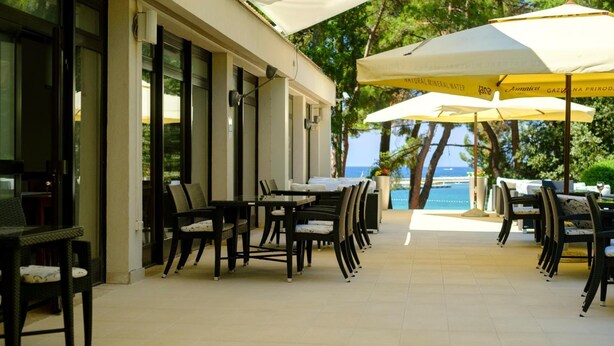 An outdoor dining area with tables and chairs, large umbrellas, and a view of the sea. - Flores (Porec)