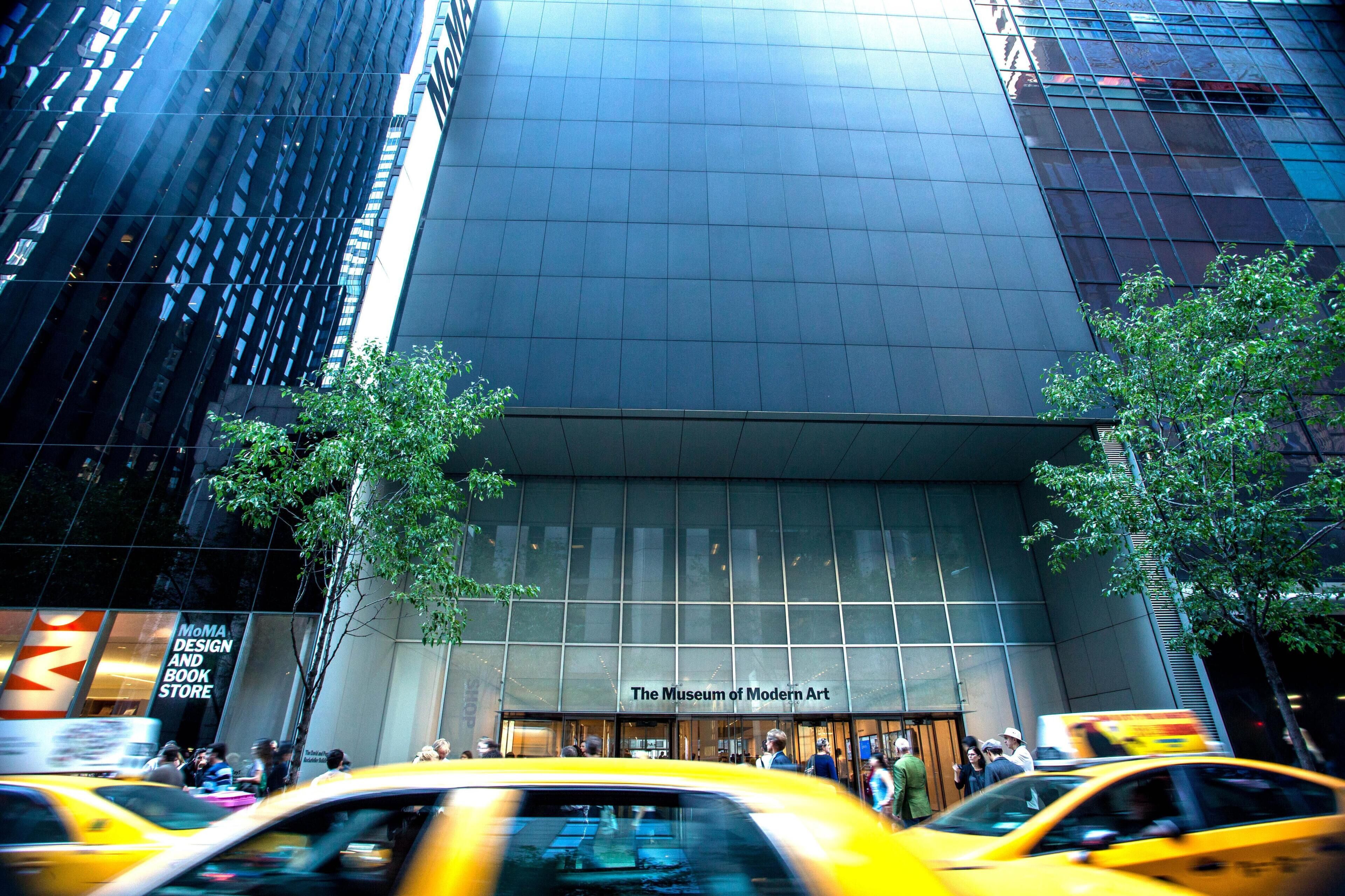 Un edificio moderno con una amplia fachada de vidrio y un cartel que dice 'The Museum of Modern Art'.