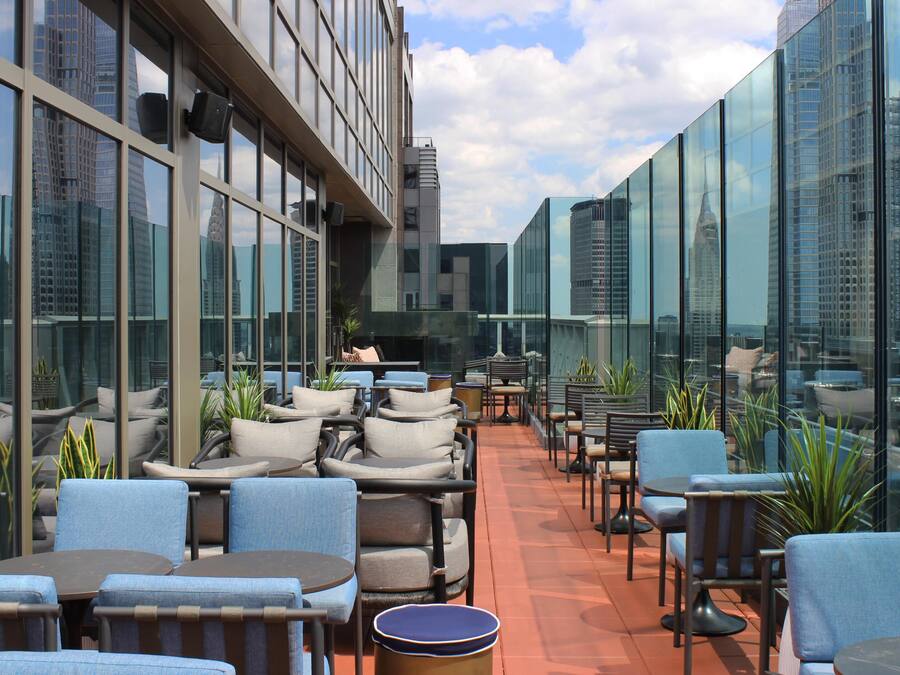 A rooftop terrace with outdoor seating, large windows, and a view of the city skyline.