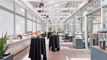 Un vaste espace intérieur aménagé avec des tables et des chaises, de grandes fenêtres et des ventilateurs de plafond.