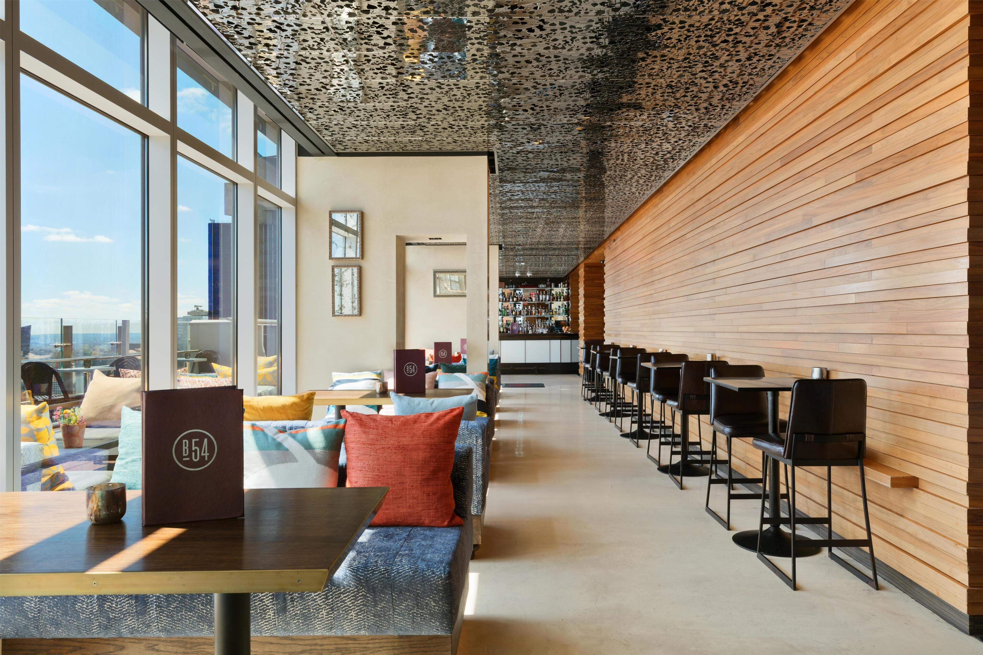 A modern hotel lobby with a long reception desk, seating area, and large windows offering city views.
