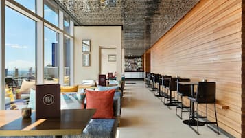 A modern hotel lobby with a long reception desk, seating area, and large windows offering city views.